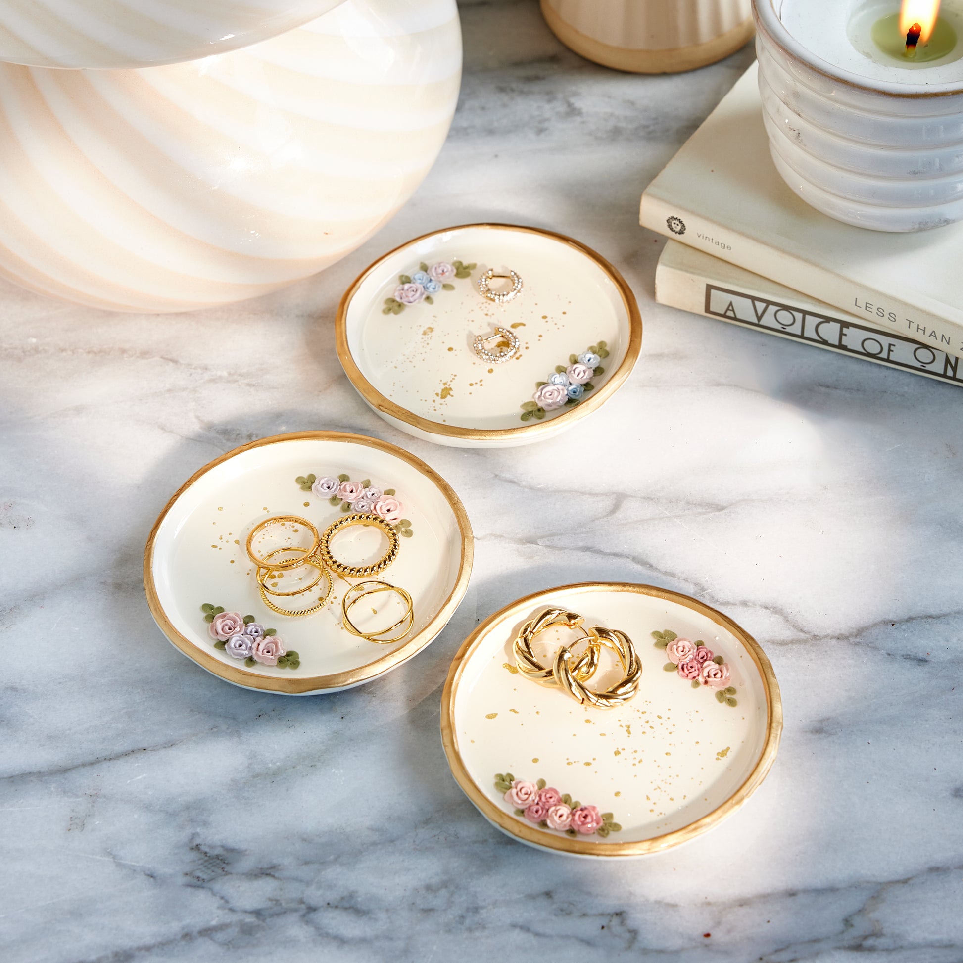 Set of three decorative jewelry trays with floral designs on a marble surface.