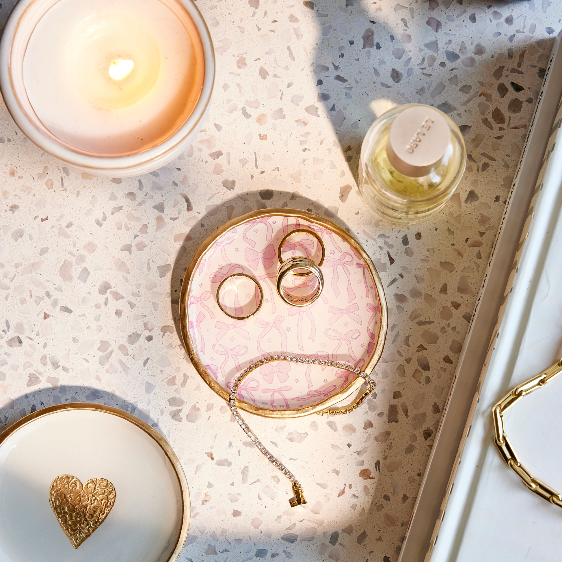 Pink Bows ring dish and a necklace on the decorative tray with a candle and perfume bottle in the background.