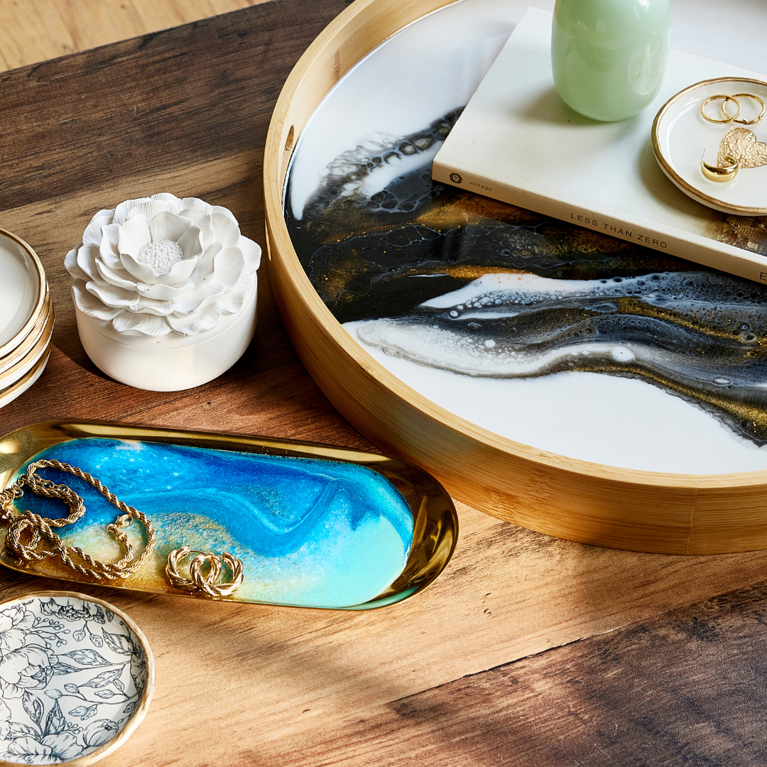 Decorative items including a white ceramic flower, gold jewelry dish, and a round wooden tray with a marble-like design on a wooden surface.