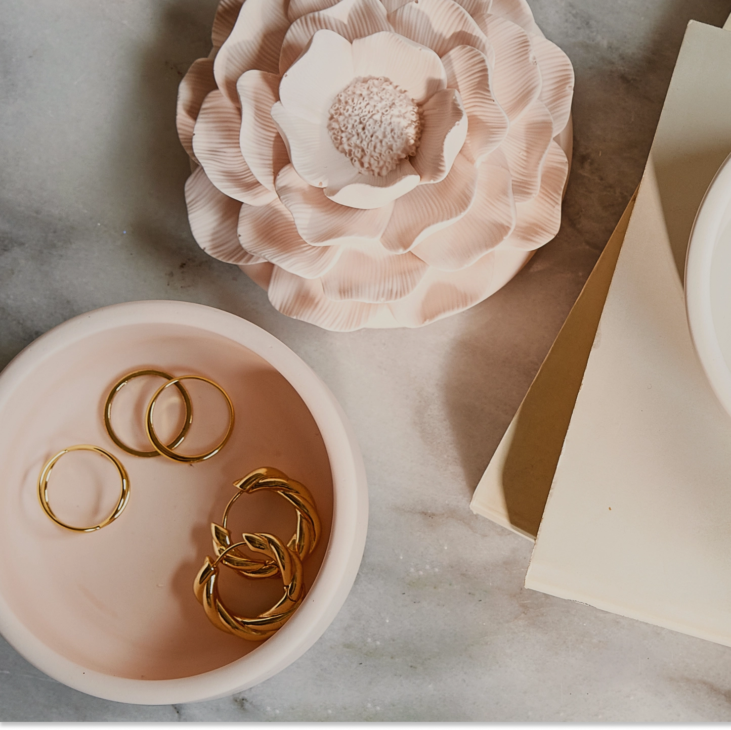 Gold rings in a bowl with decorative flowers on a marble surface