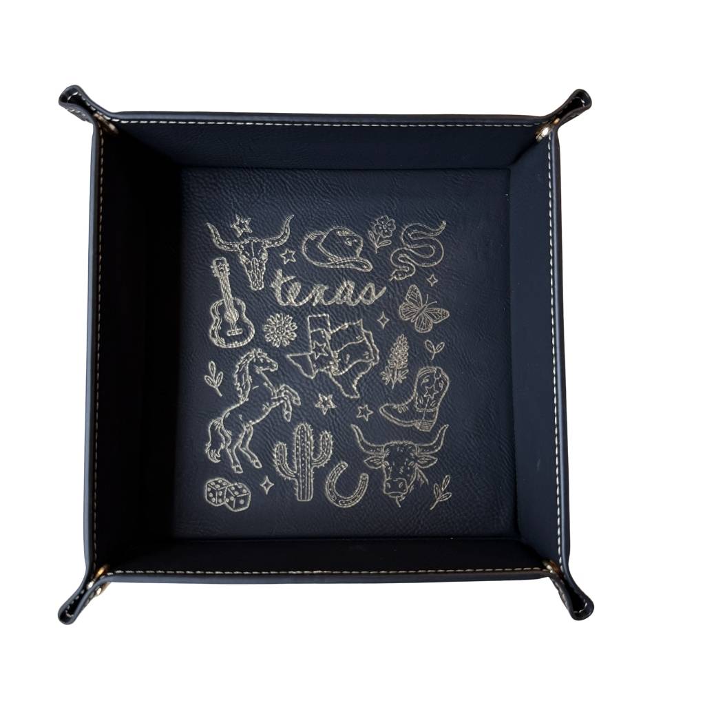 Black leatherette valet tray with laser-engraved Texas illustration including longhorn skull, cowboy hat, cowboy boots, cactus, and guitar, folded open on a light wood surface
