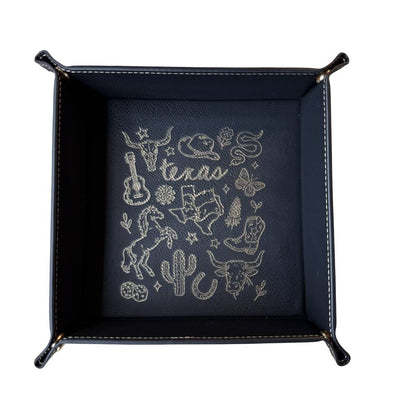 Black leatherette valet tray with laser-engraved Texas illustration including longhorn skull, cowboy hat, cowboy boots, cactus, and guitar, folded open on a light wood surface
