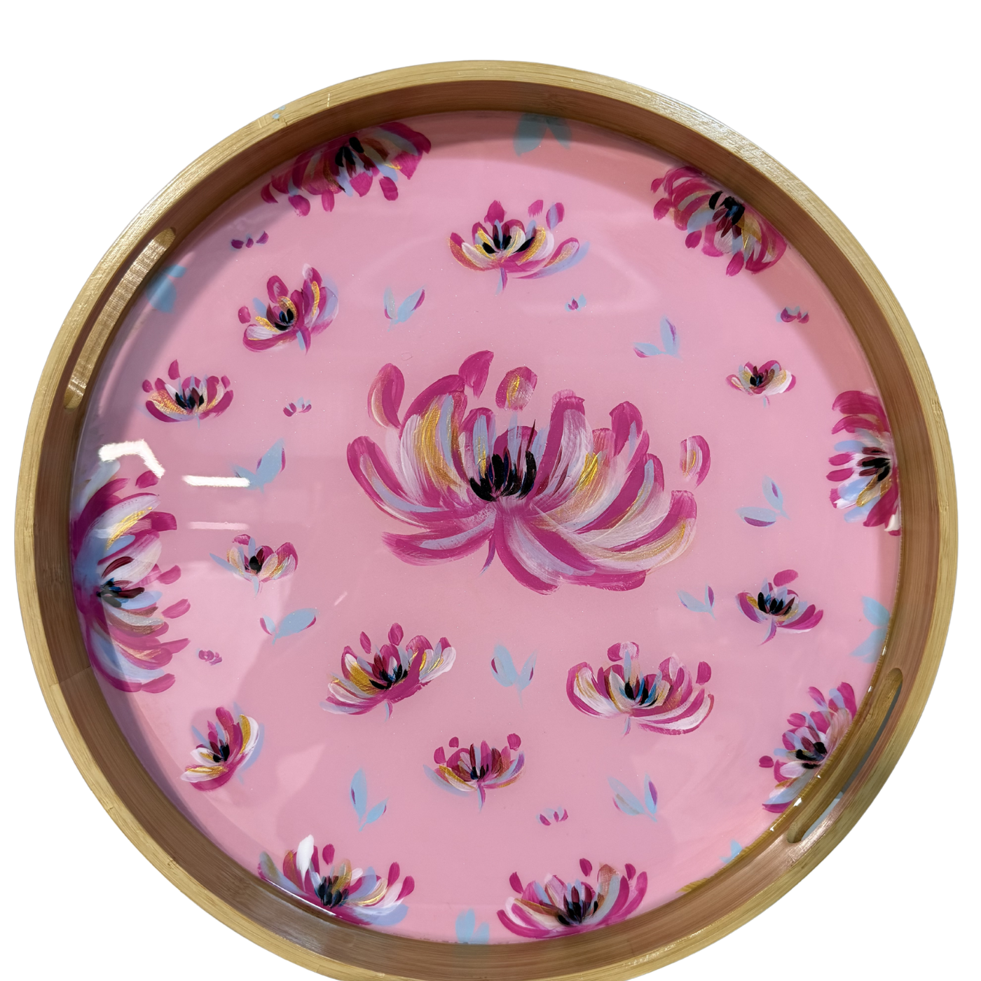 A round wooden serving tray with a glossy pink floral print, featuring painted pink flowers with yellow, white, and black details, and small blue leaf accents, framed by a natural wood rim.