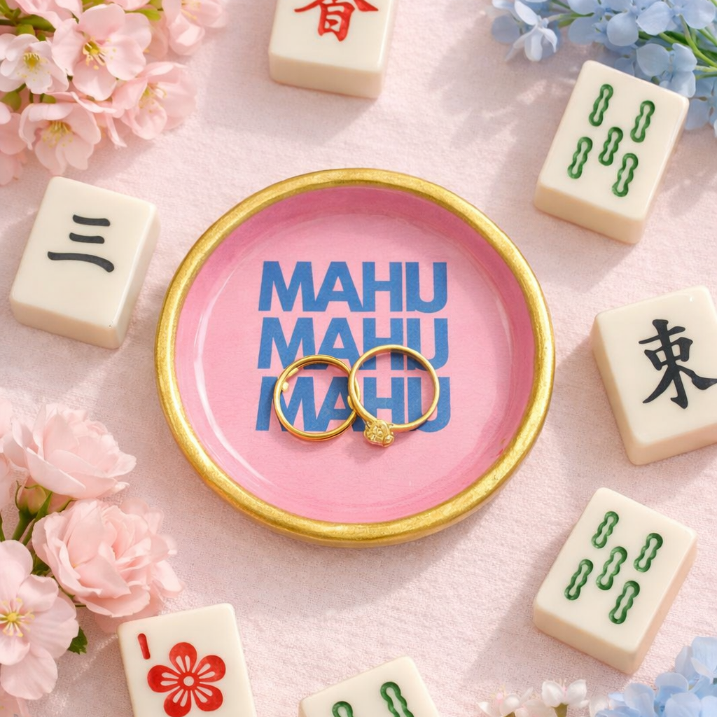 Pink ring dish with 'MAHJ MAHJ' text surrounded by decorative tiles and flowers on a pink background
