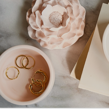 Gold rings in a bowl with decorative flowers on a marble surface
