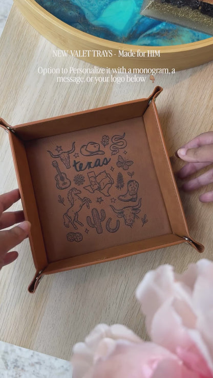 leatherette valet tray with laser-engraved Texas illustration including longhorn skull, cowboy hat, cowboy boots, cactus, and guitar, folded open on a light wood surface