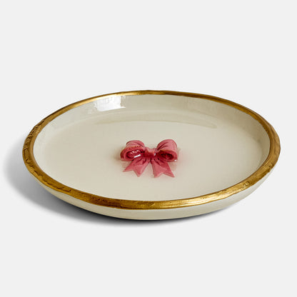 Beige ring dish with gold rim featuring a pink bow on a white background
